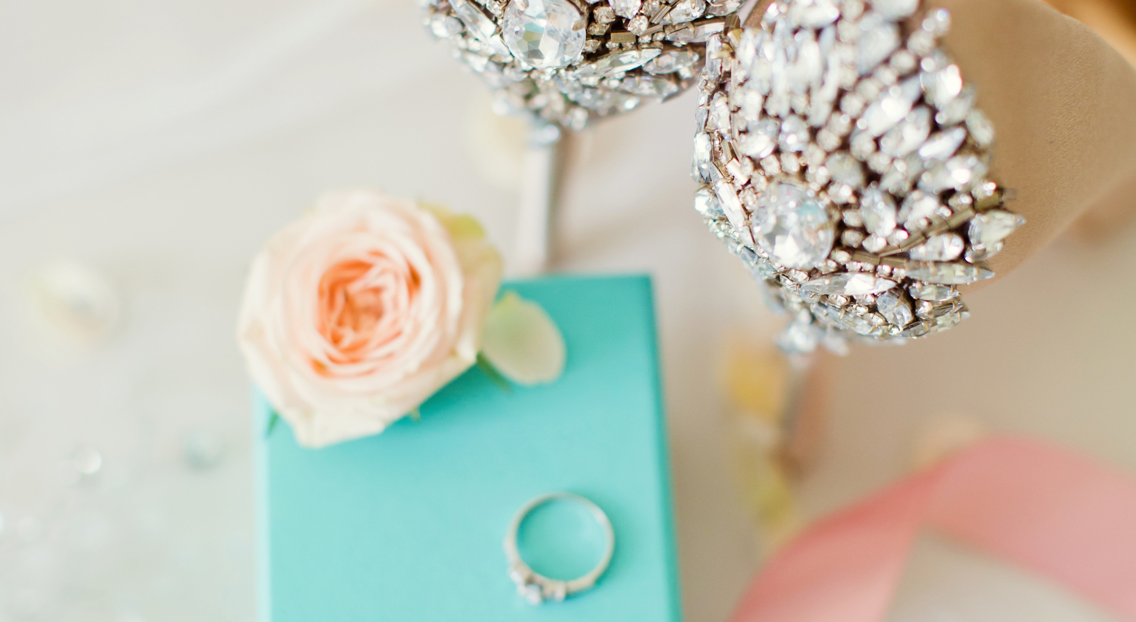 Wedding shoes and an engagement ring on a blue box next to a flower