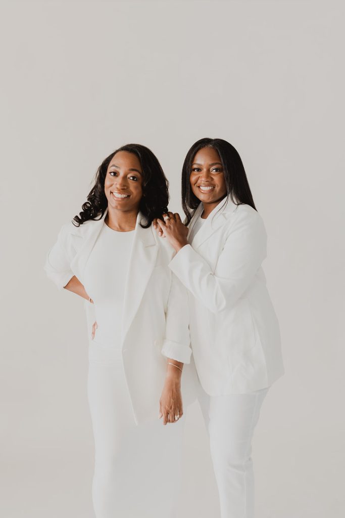 Two African American women in all white outfits stare at the camera