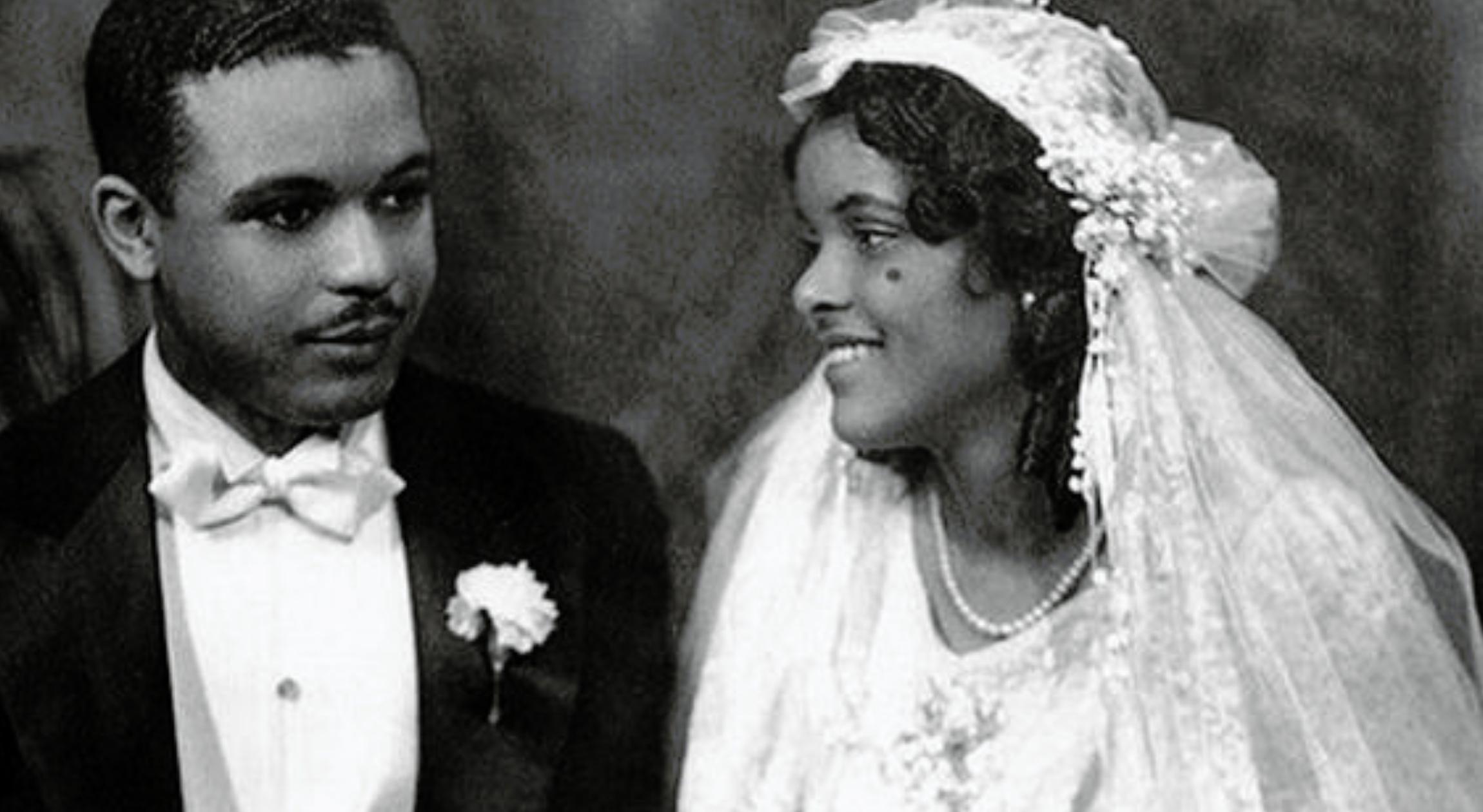A black and white photo of a Black man in a tuxedo and a Black woman in a white dress and a veil