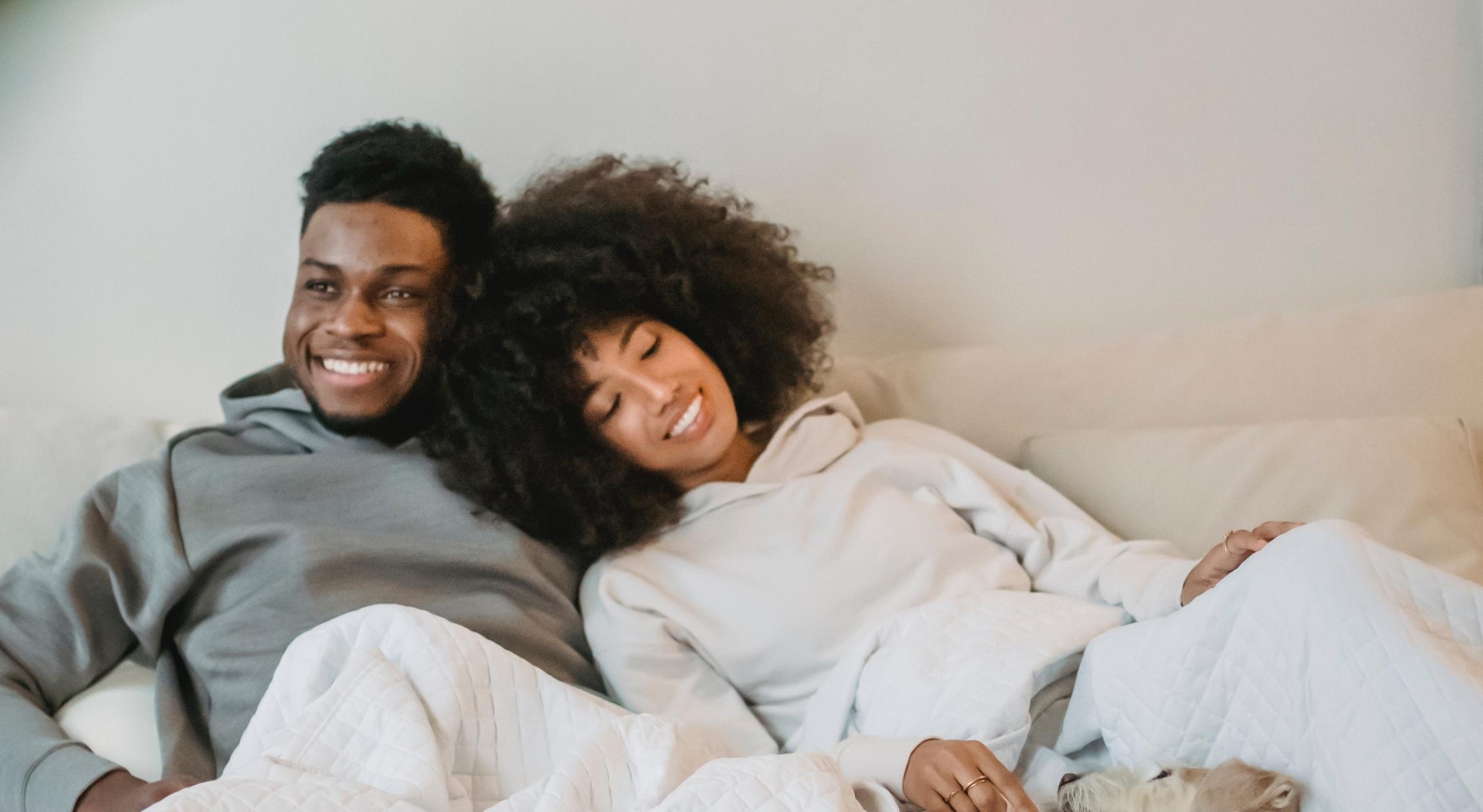 A Black couple on a bed in hoodies
