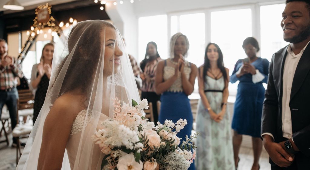 A woman in bridal wear approaches a man in a suit in front of people