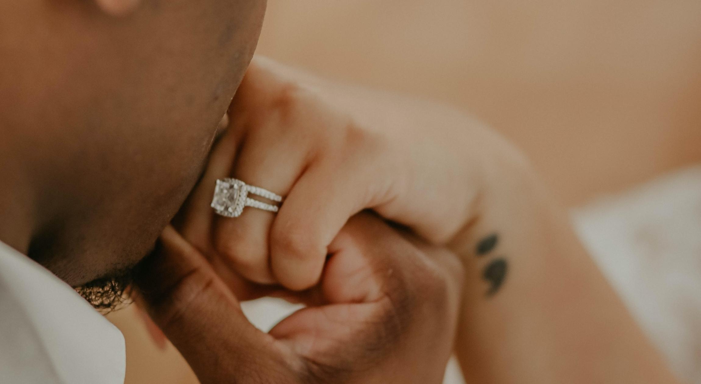 A Brown hand with an engagement ring is kissed