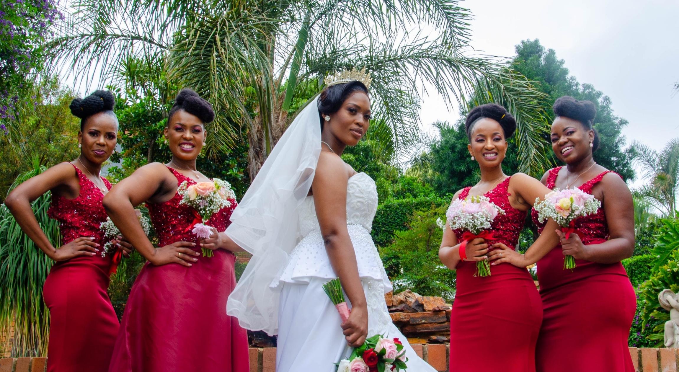 Four Black bridesmaids in red dresses surrounding a Black bride