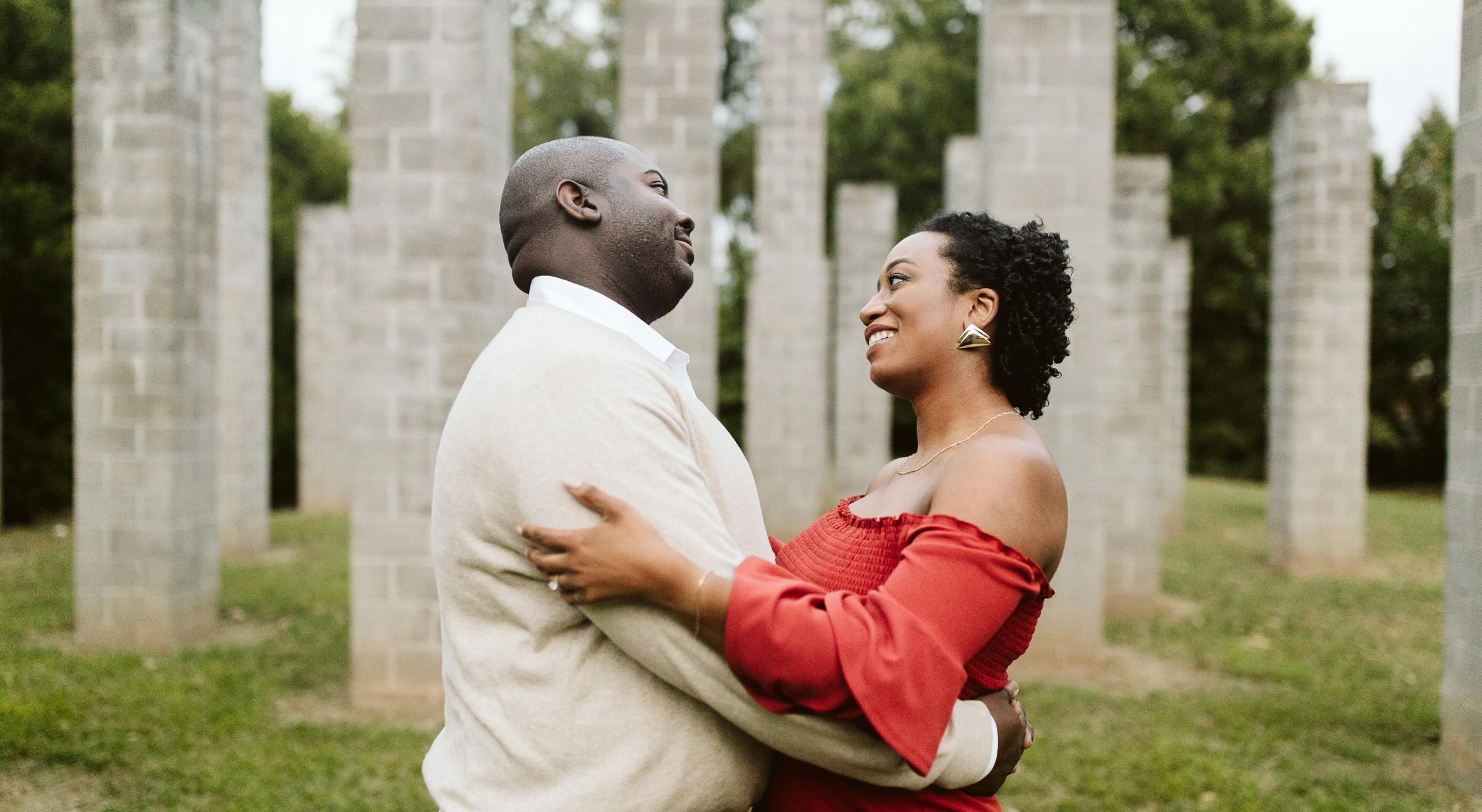 A Black couple in a park staring at each other as they embrace