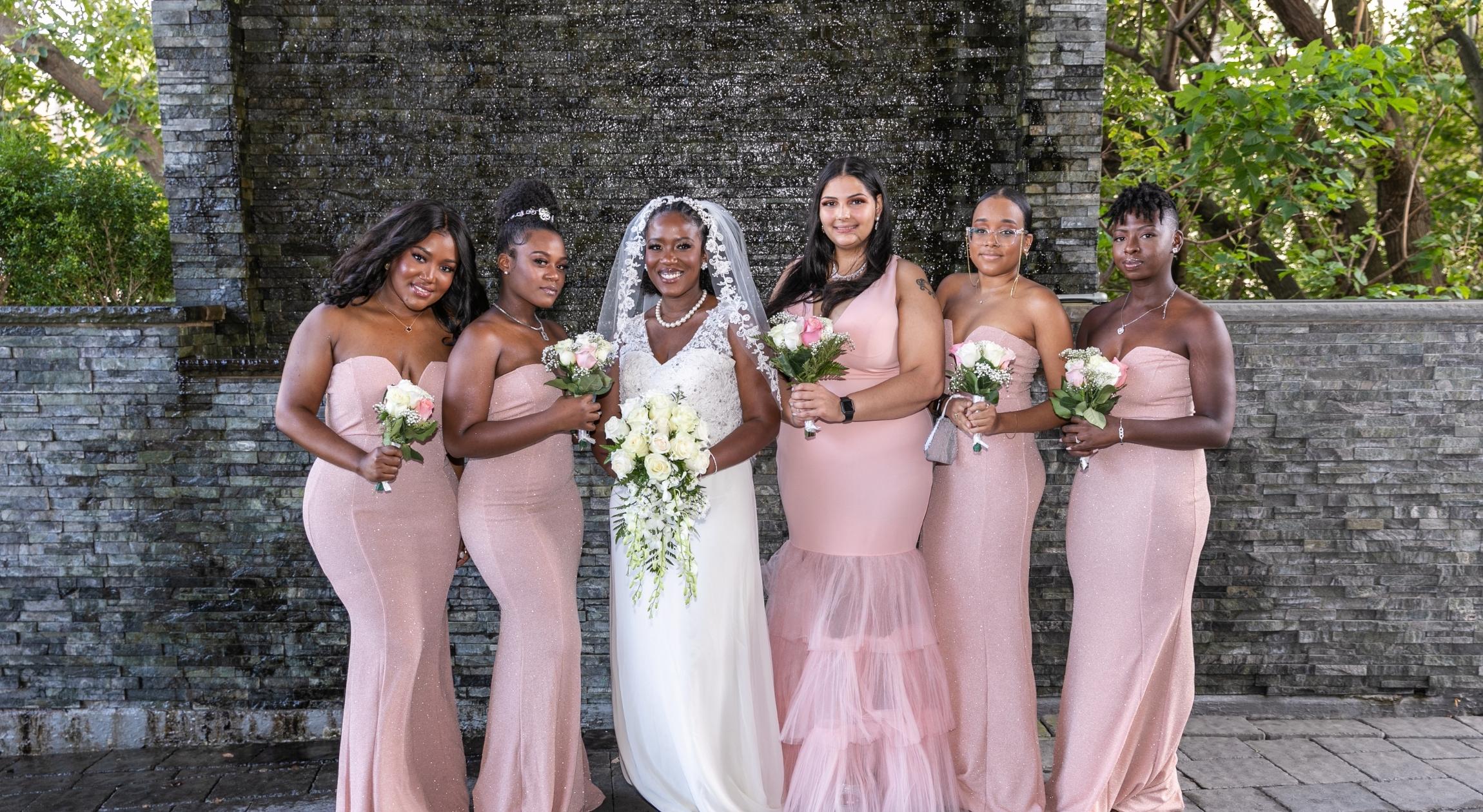Five bridesmaids in pink dresses surrounded by a Haitian bride