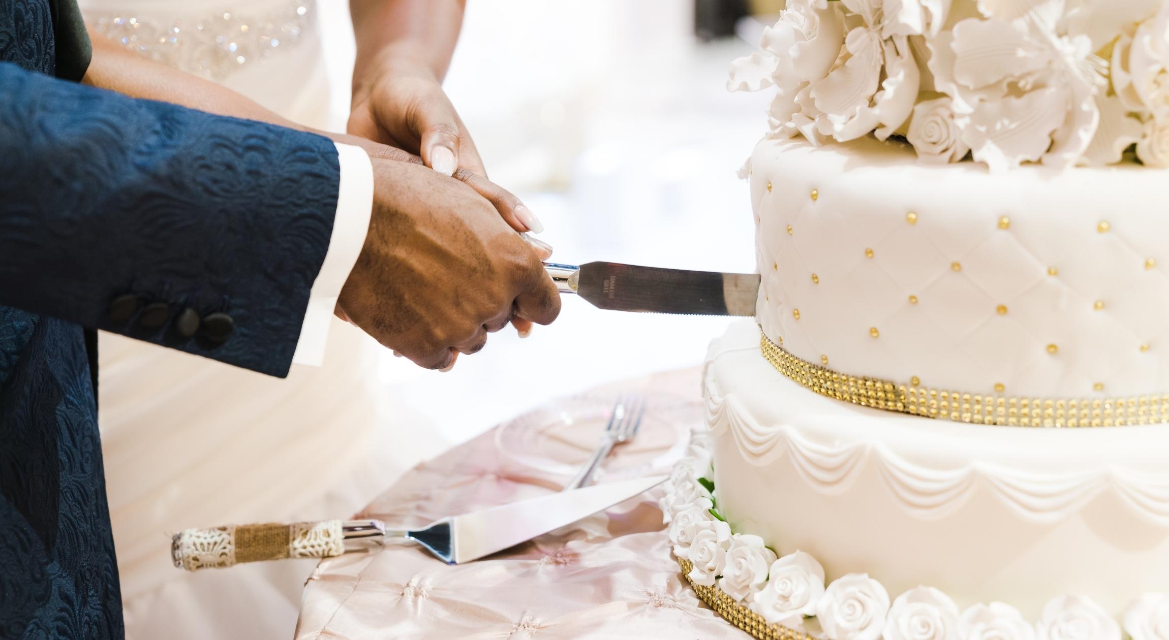 The hands of a Black couple cutting into a wedding cake
