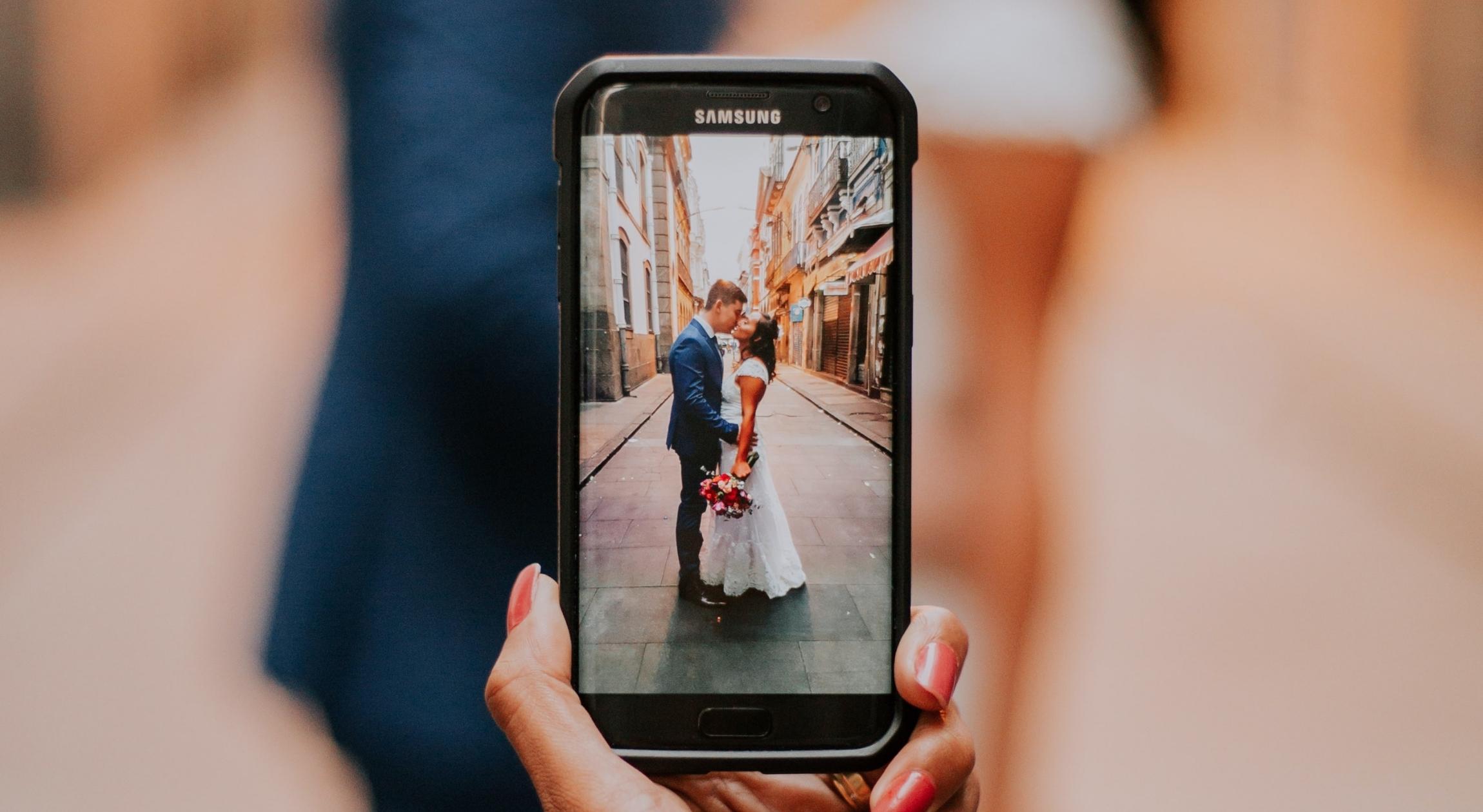 A cell phone capturing a couple in wedding clothes