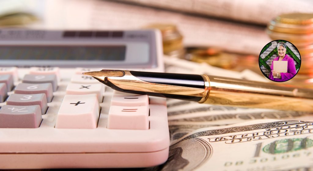 A pink calculator on a table. A gold pen rests on top of the calculator. Money is in the foreground.