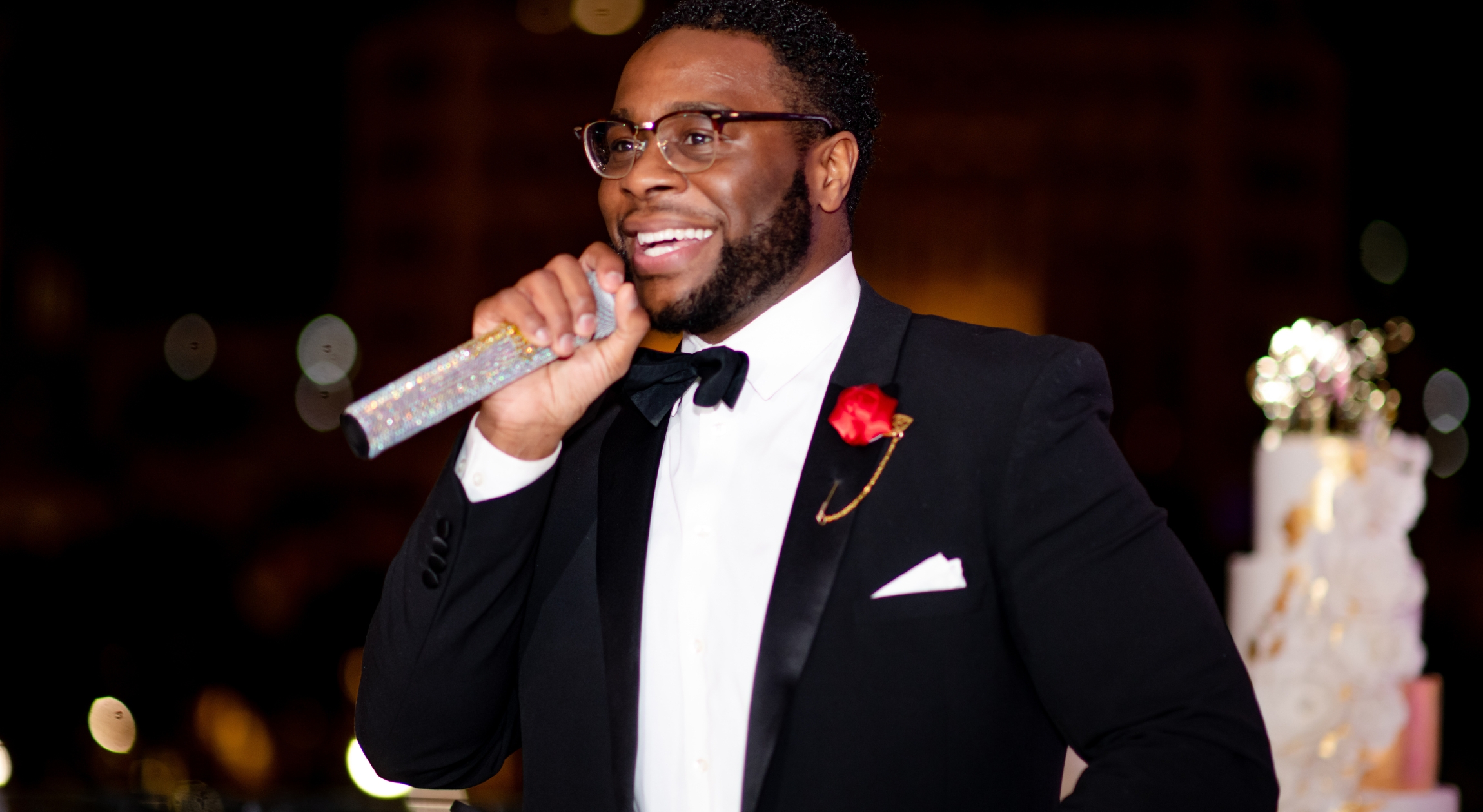 A Black man in a tuxedo holding a microphone