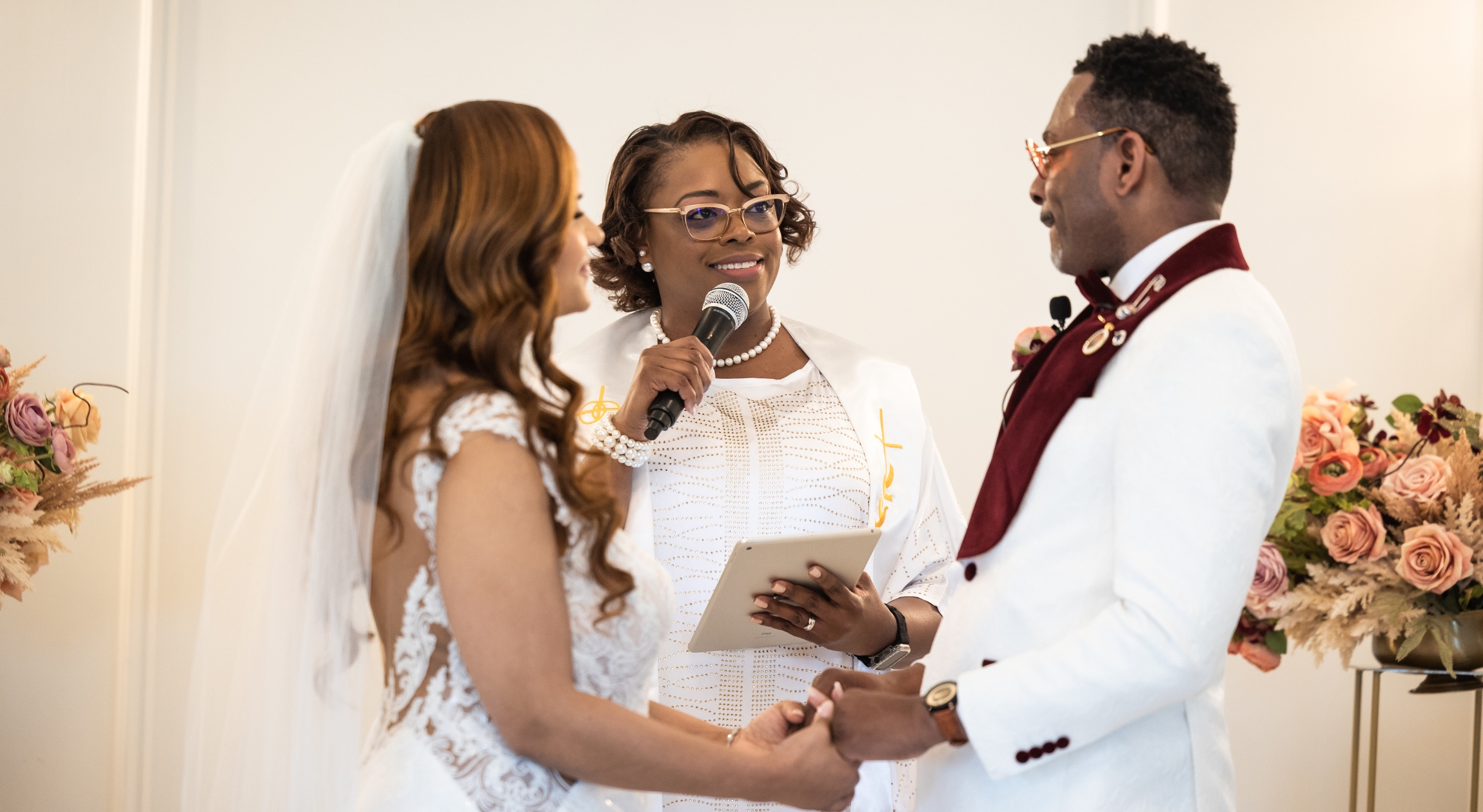 A Black wedding officiant stands between a bride and groom