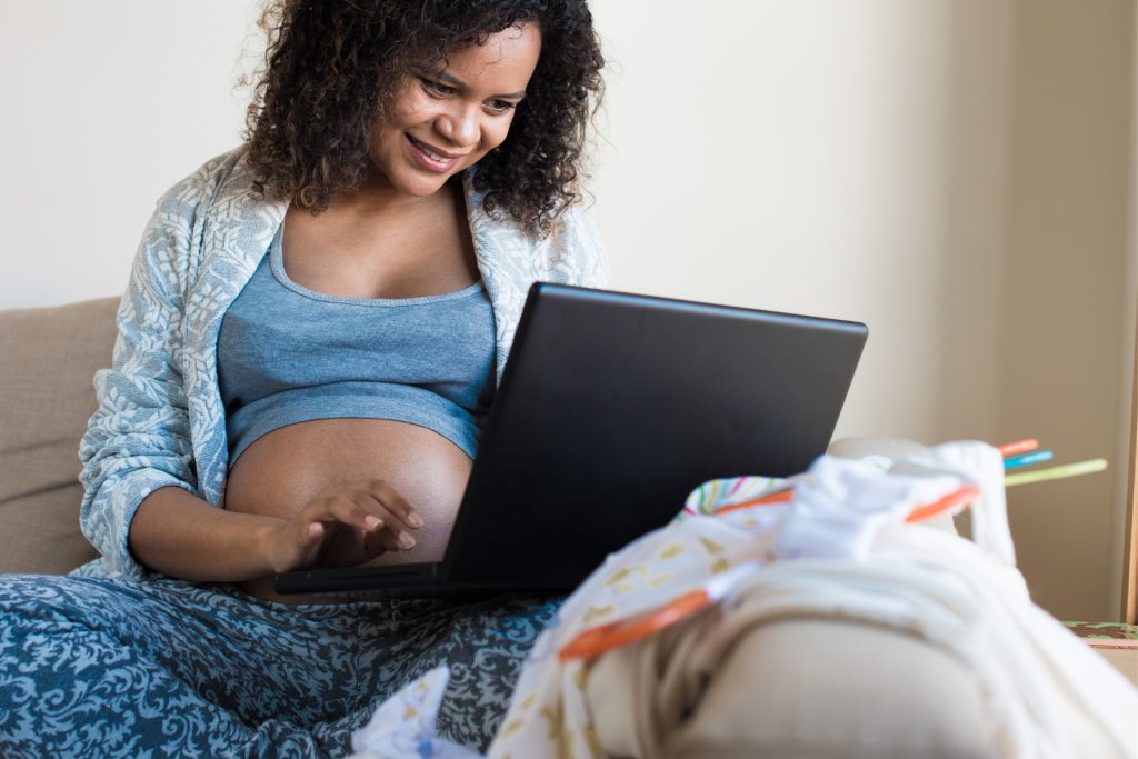 a pregnant person sitting on a couch with a laptop