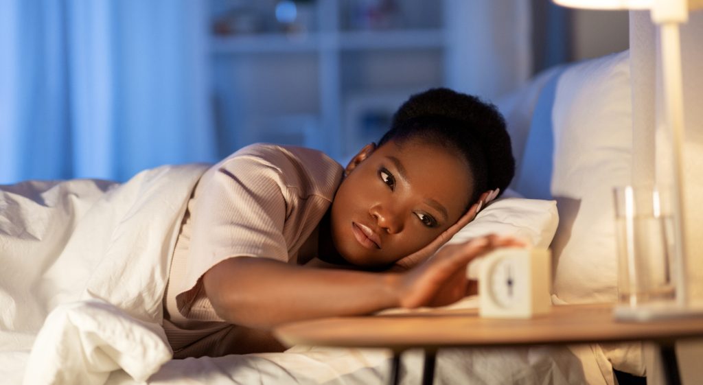 A Black woman lying in bed touches a clock