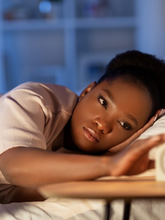 A Black woman lying in bed touches a clock