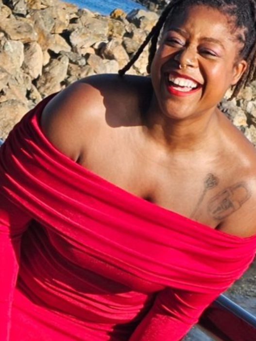 a person in a red dress smiling by the water