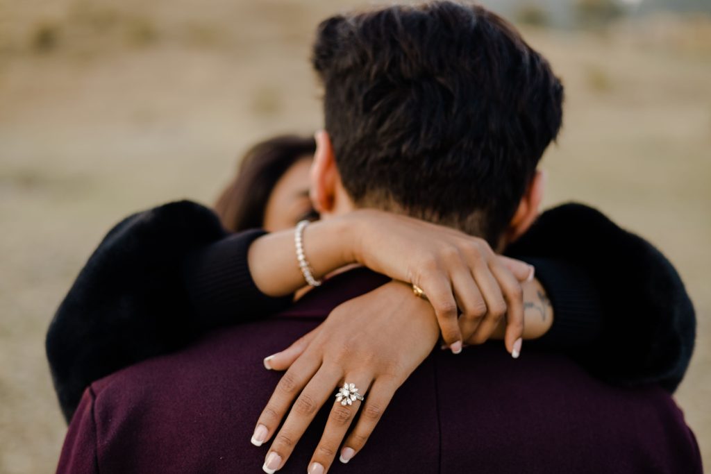 An engaged couple hugging in the middle of the field