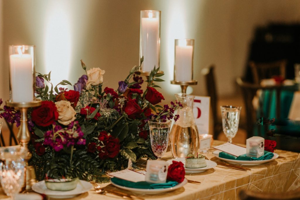 a table setting with red and gold flowers and candles