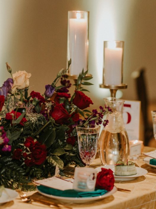 a table setting with red and gold flowers and candles