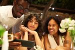 A wedding content creator vs. guest is at a table looking at a cell phone with the couple of honor.