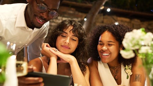 A wedding content creator vs. guest is at a table looking at a cell phone with the couple of honor.
