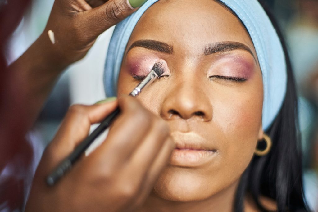 a Black woman getting her makeup done by a makeup artist