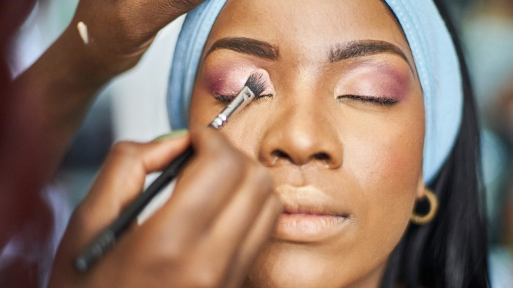 a Black woman getting her makeup done by a makeup artist
