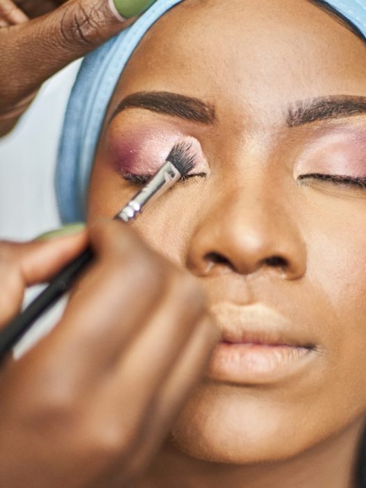 a Black woman getting her makeup done by a makeup artist