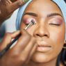 a Black woman getting her makeup done by a makeup artist