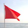 a red flag on the beach with the ocean in the background