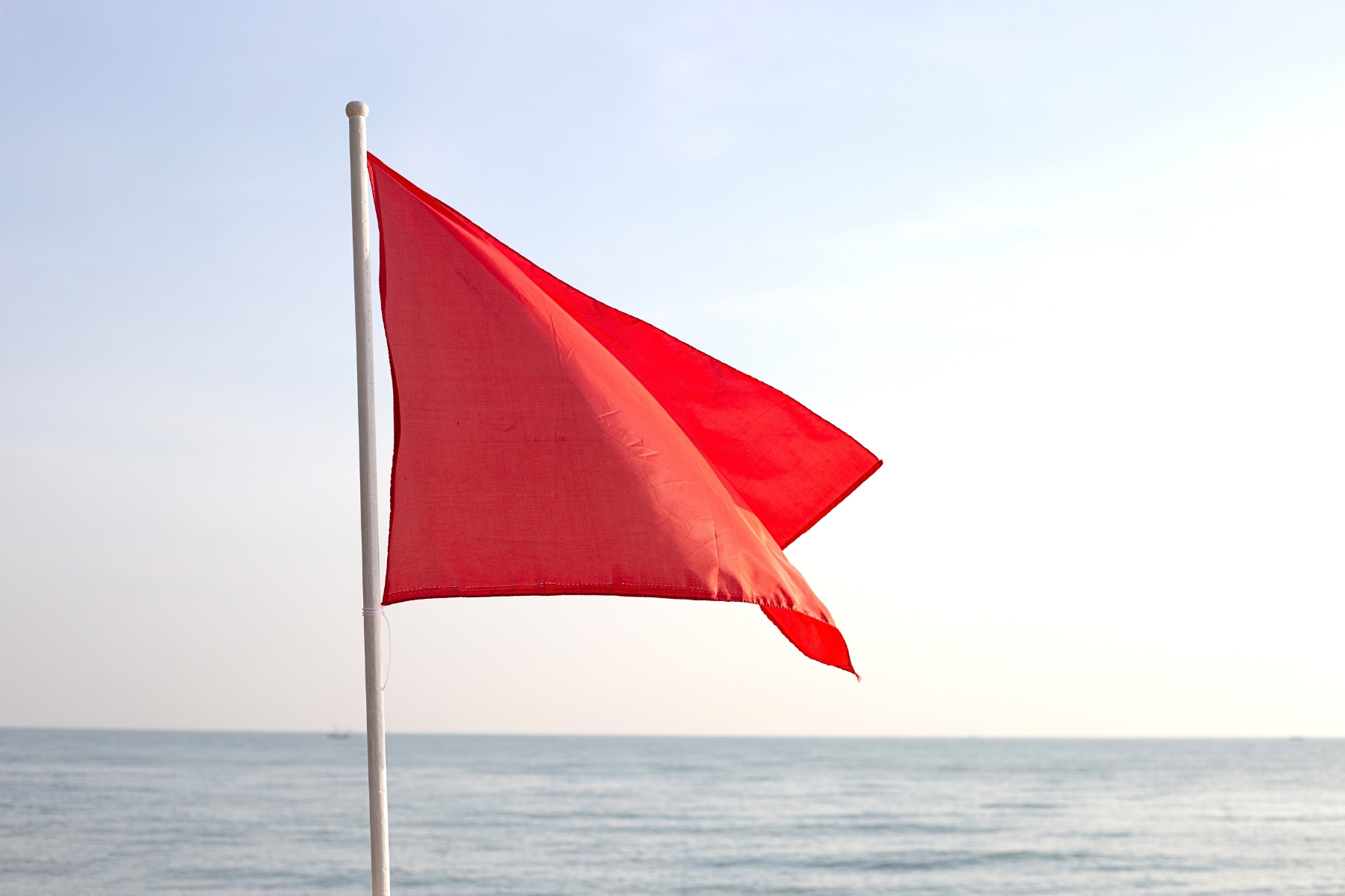 a red flag on the beach with the ocean in the background