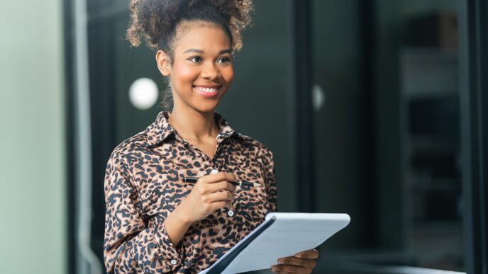 A smiling person in a leopard print shirt holds a pen and a notepad, looking to the side.