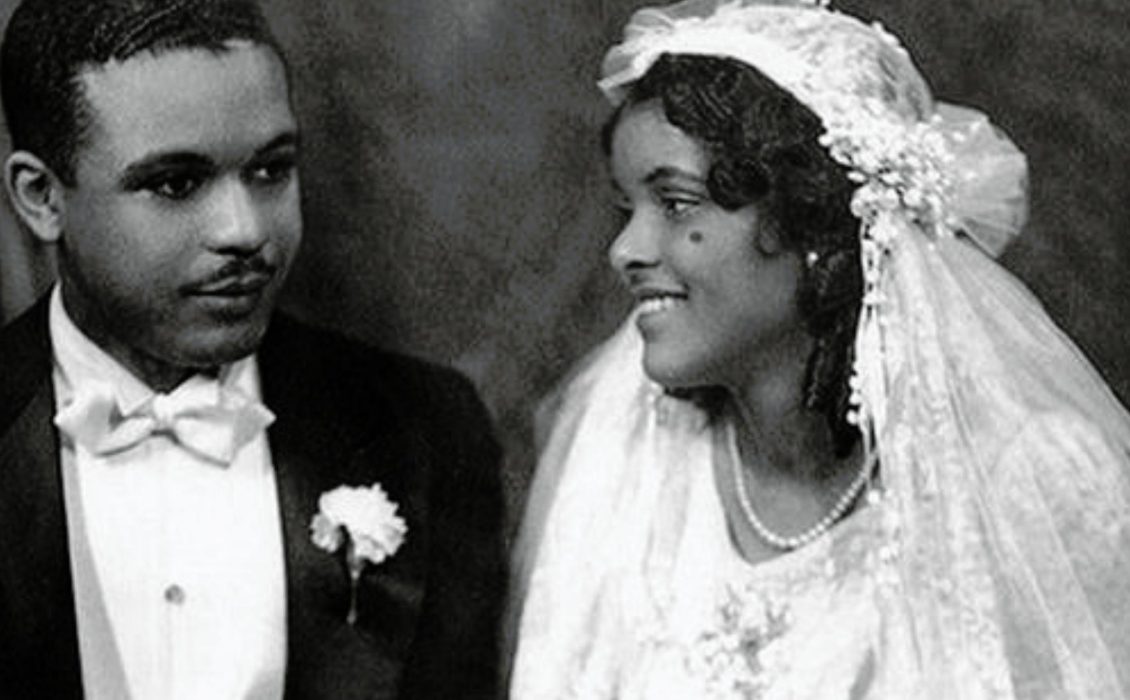 A black and white photo of a Black man in a tuxedo and a Black woman in a white dress and a veil