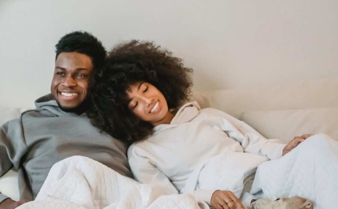 A Black couple on a bed in hoodies