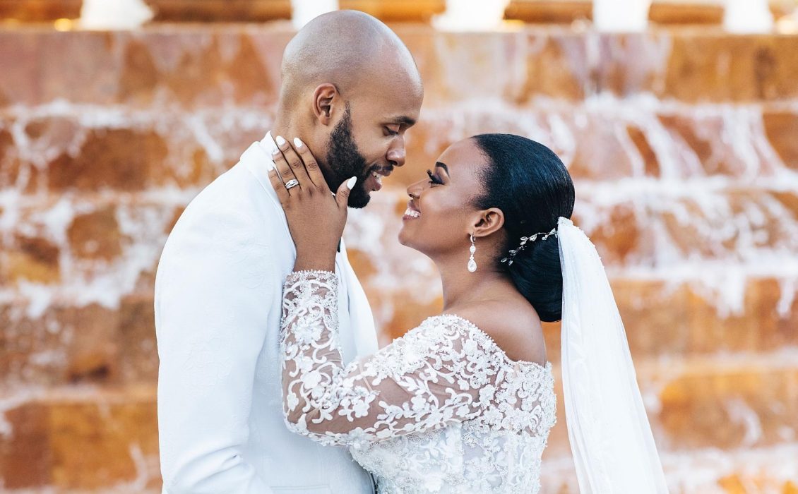 A Black married couple in their wedding attire facing each other lovingly