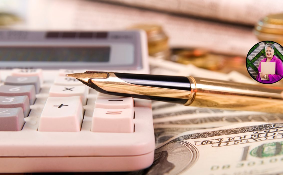 A pink calculator on a table. A gold pen rests on top of the calculator. Money is in the foreground.