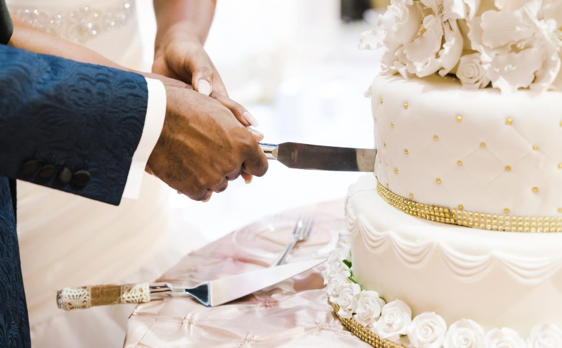 The hands of a Black couple cutting into a wedding cake