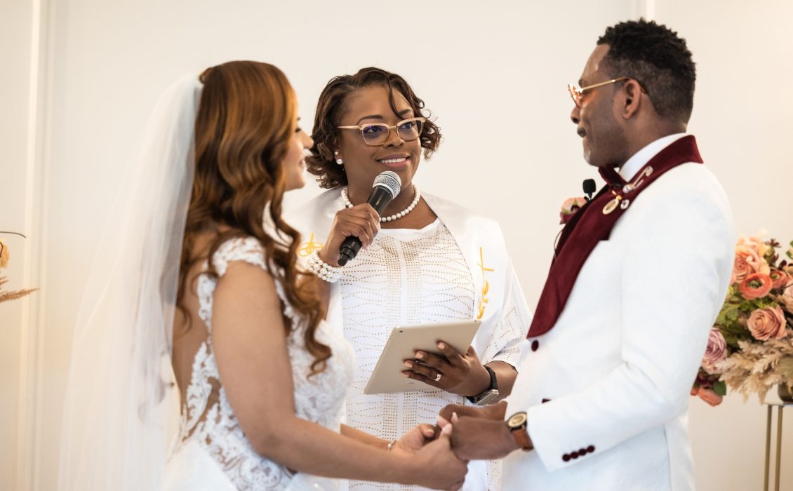 A Black wedding officiant stands between a bride and groom